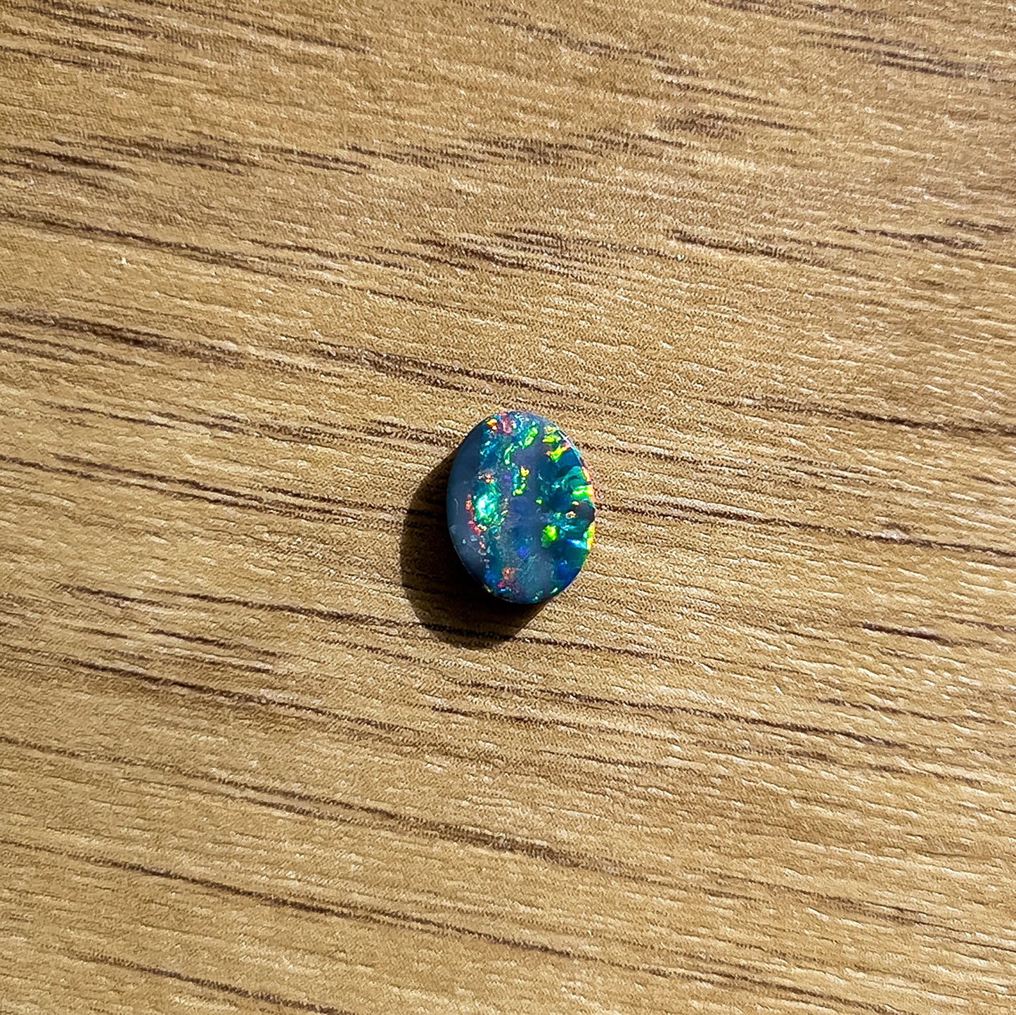 A Loose Doublet Opal with an oval cut, measuring 9mm x 7mm. The opal displays an impressive array of bright red, green, and blue hues, with occasional flashes of radiant orange | Opalist
