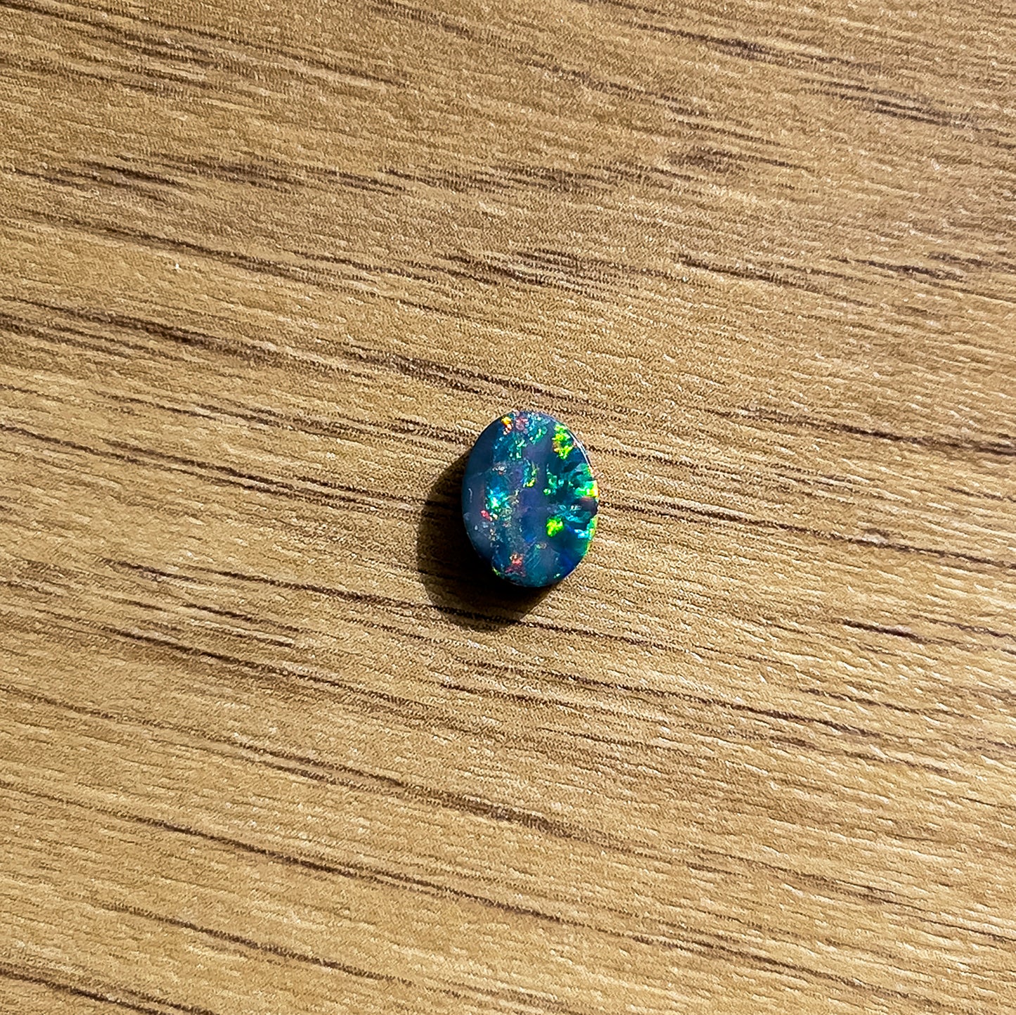 A Loose Doublet Opal with an oval cut, measuring 9mm x 7mm. The opal displays an impressive array of bright red, green, and blue hues, with occasional flashes of radiant orange | Opalist