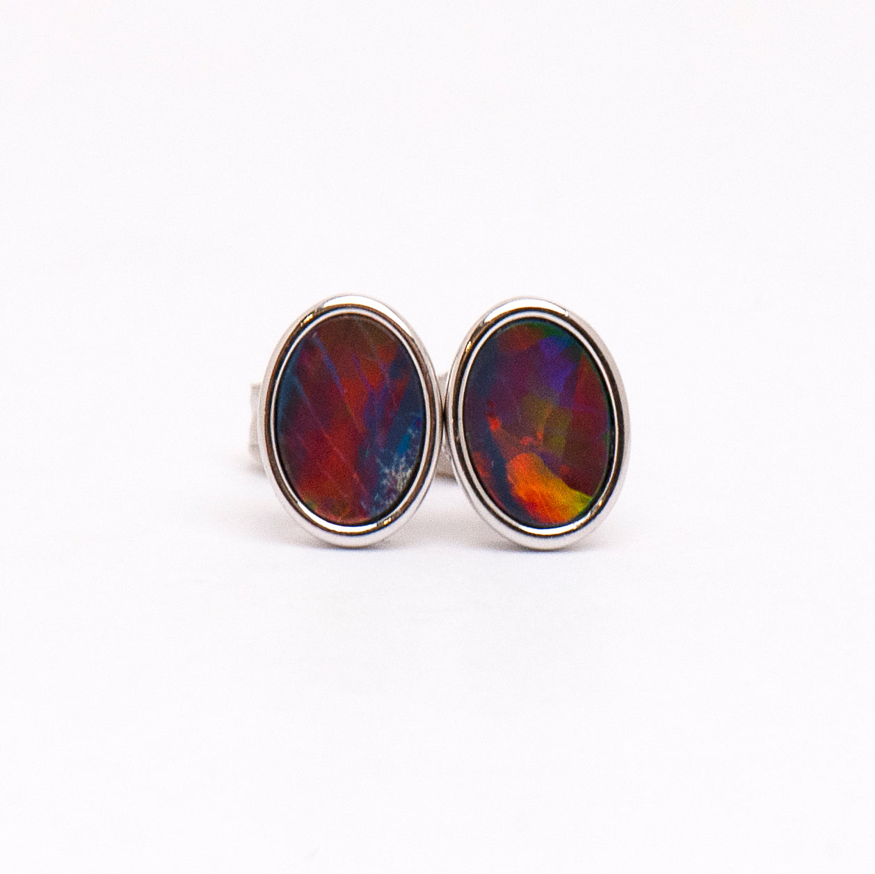 Vibrant Sterling Silver Doublet Opal Stud Earrings from Opalist. Oval-cut opal doublets showcase a mesmerizing play of colors, including vibrant reds, greens, and blues with a touch of purple. The earrings are bezel set for a secure and stylish design | Opalist