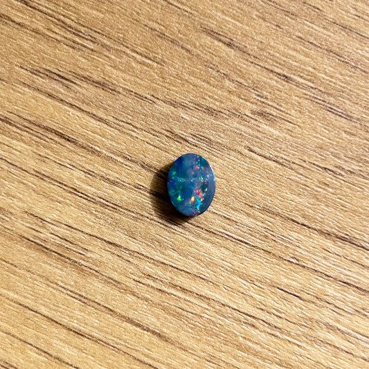 A Loose Doublet Opal with an oval cut, measuring 9mm x 7mm. The opal displays an impressive array of bright red, green, and blue hues, with occasional flashes of radiant orange | Opalist